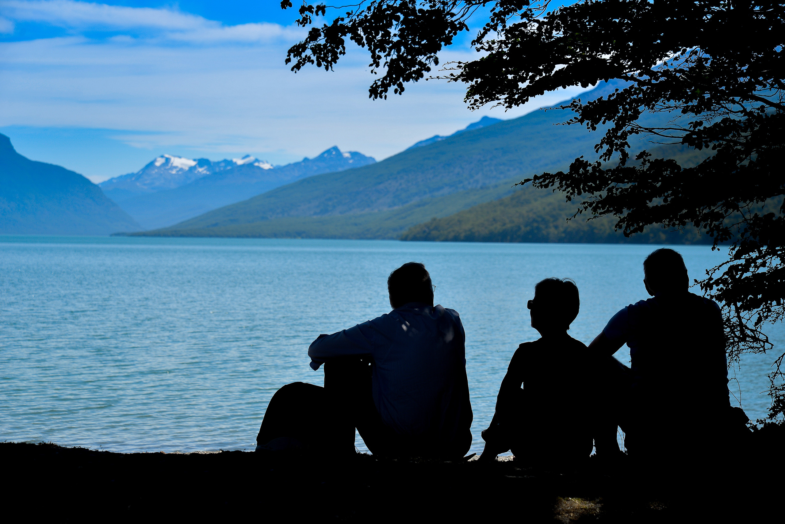 Siluetas de visitantes frente a un lago y montañas en el Parque Nacional Tierra del Fuego