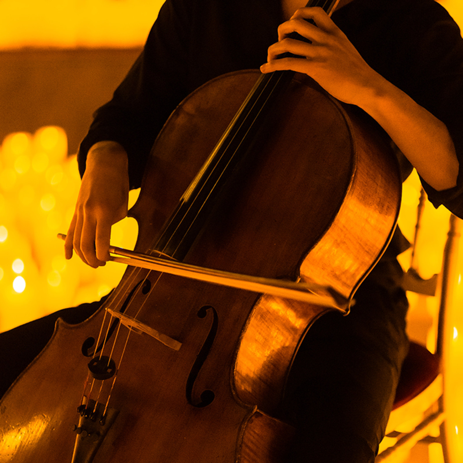 Violoncellista tocando entre velas en un concierto Candlelight