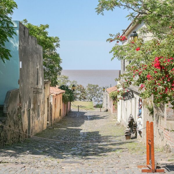 Calle empedrada del Barrio Histórico de Colonia del Sacramento con buganvilias y el Río de la Plata al fondo