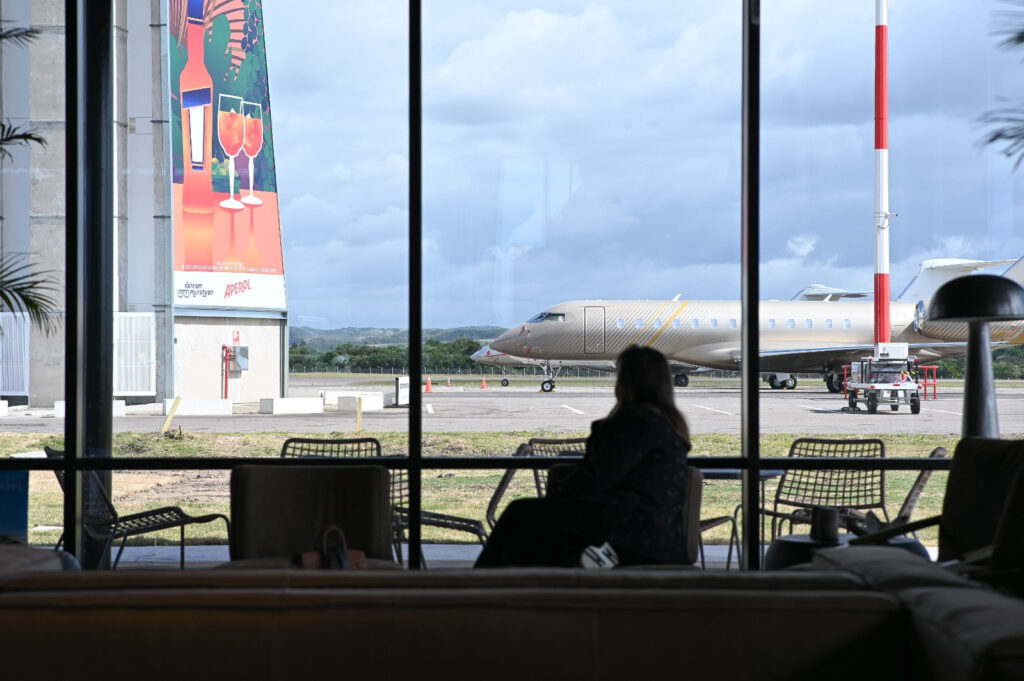Pasajera frente a los ventanales de la terminal con un jet privado en la plataforma
