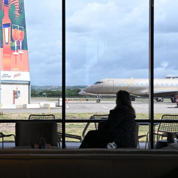 Pasajera frente a los ventanales de la terminal con un jet privado en la plataforma