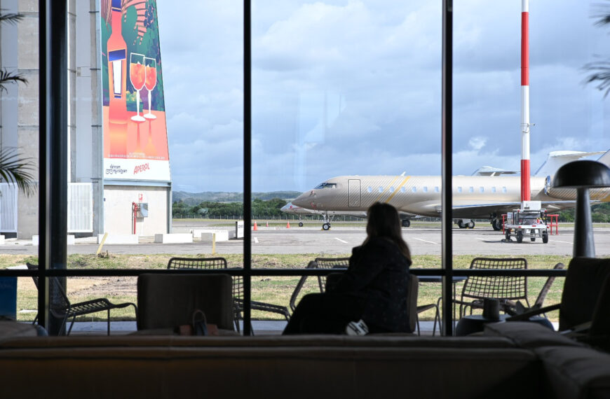 Pasajera frente a los ventanales de la terminal con un jet privado en la plataforma